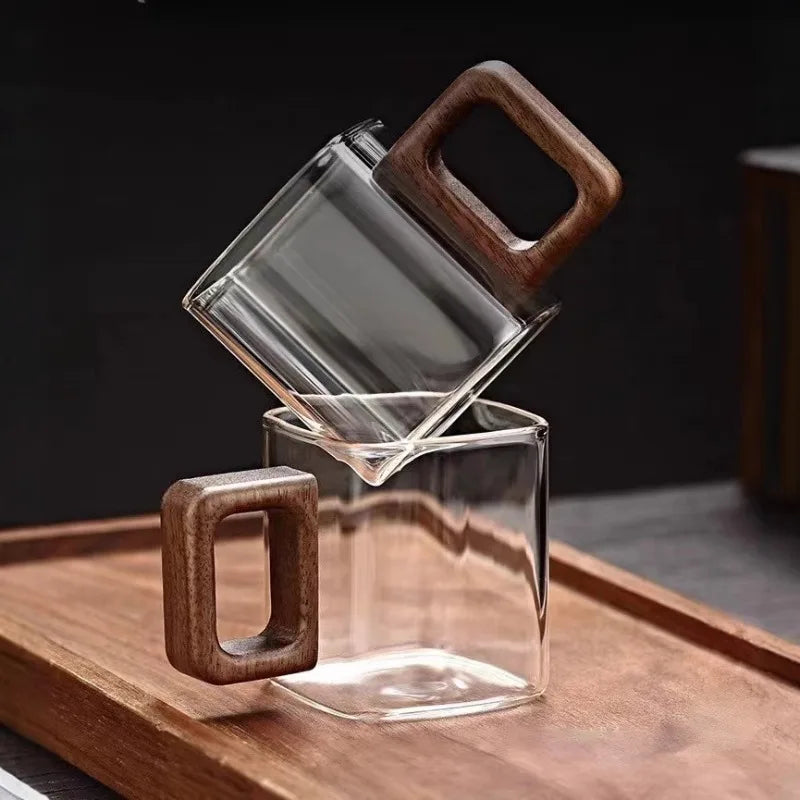 Two clear square borosilicate glass mugs with premium walnut wood handles stacked vertically to show design stability.
