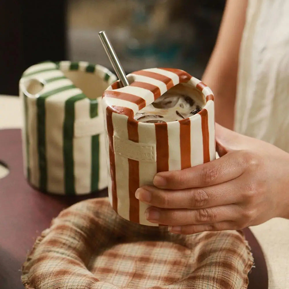 Person holding a striped ceramic mug with another mug in the background