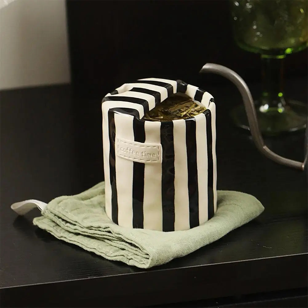 Black and white striped kettle with a green towel on a dark surface