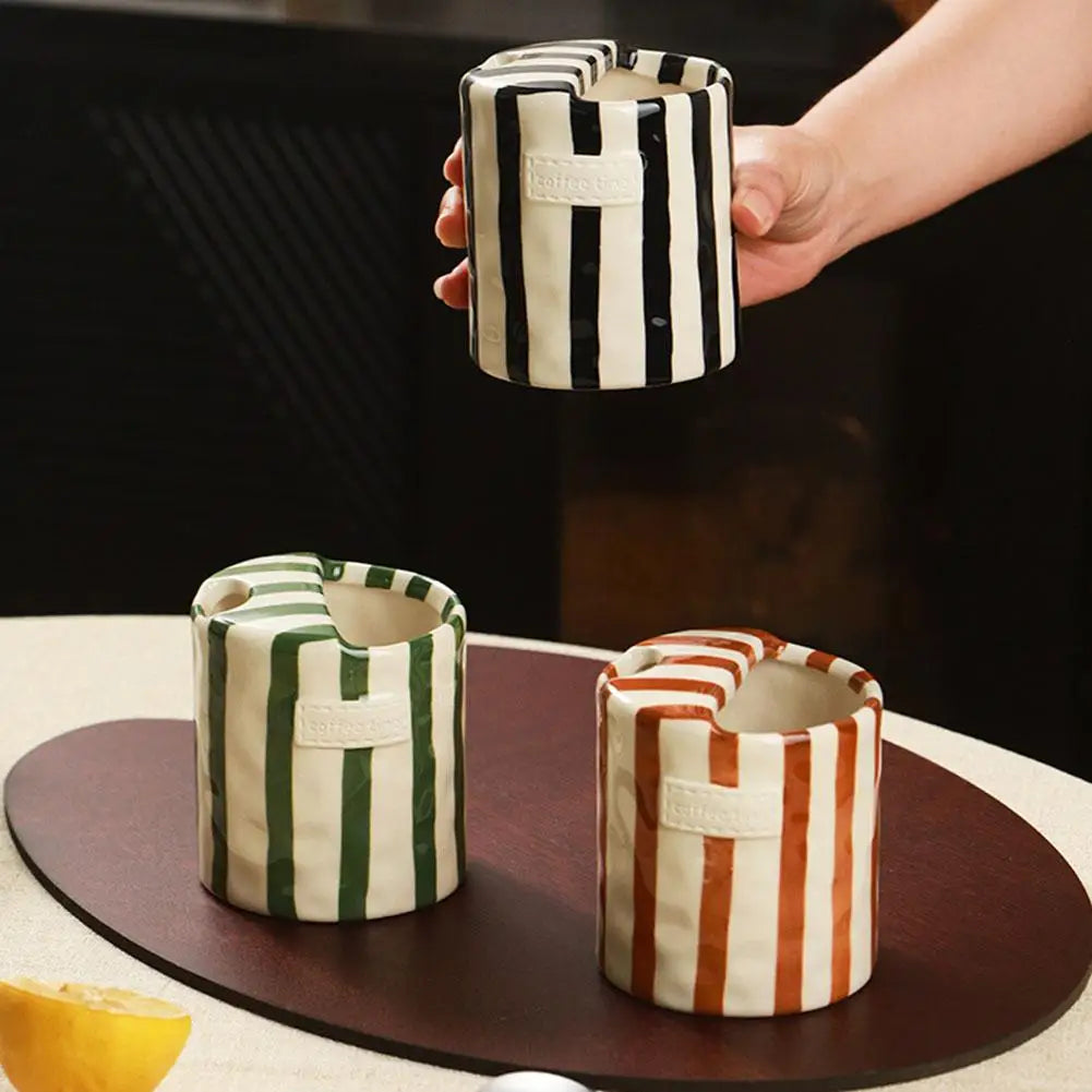A top-down aesthetic view showing a hand placing a green and brown striped ceramic mug onto a rectangular wooden serving tray.