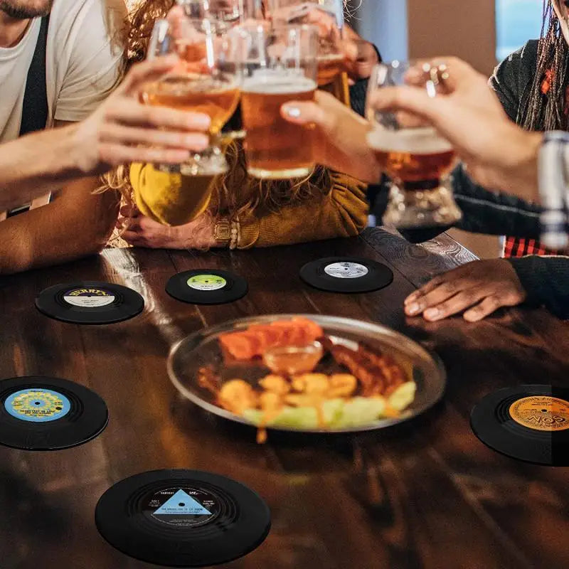 People toasting with glasses of beer at a table with vinyl record coasters and a plate of food.