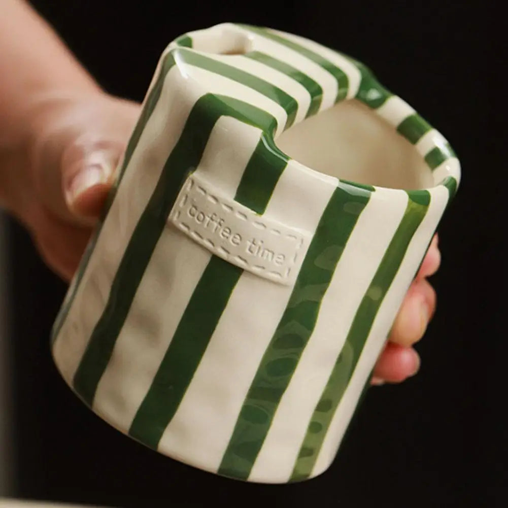 Green and white striped mug with 'coffee time' text held by a hand against a dark background
