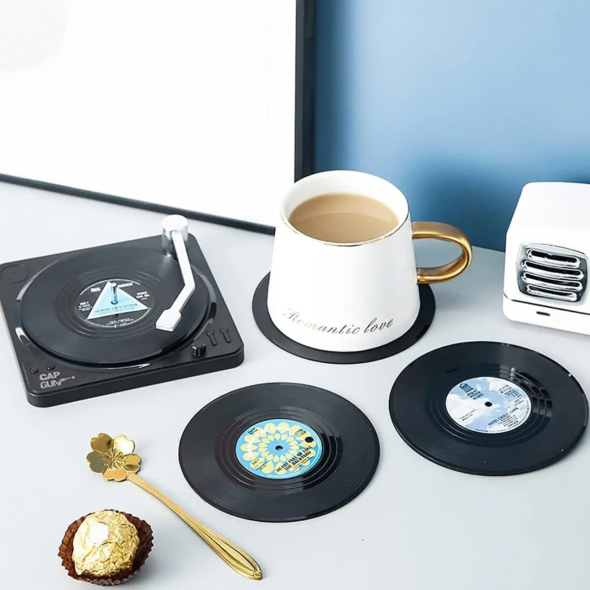 Record-style coasters with a cup of coffee and a toaster on a white surface.
